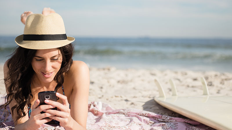 Smiling woman on sandy beach looking at phone
