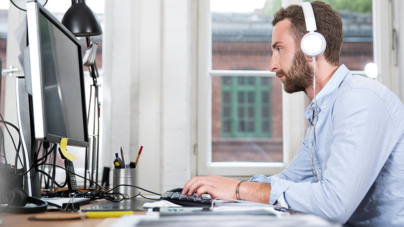 Man at desk wearing headphones looking at computer screen